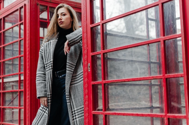 Photo a girl in a gray coat stands by a red telephone booth