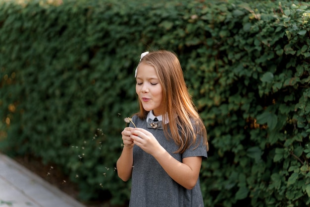 a girl in a gray dress similar to a school one blows on a dandelion