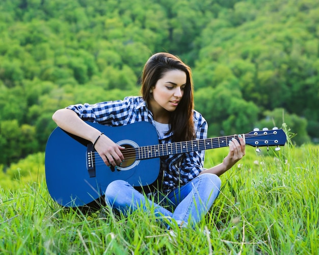 Girl on a green meadow playing guitar