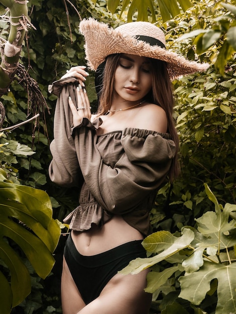 A girl in a green shirt and a straw hat in a greenhouse. Selective focus