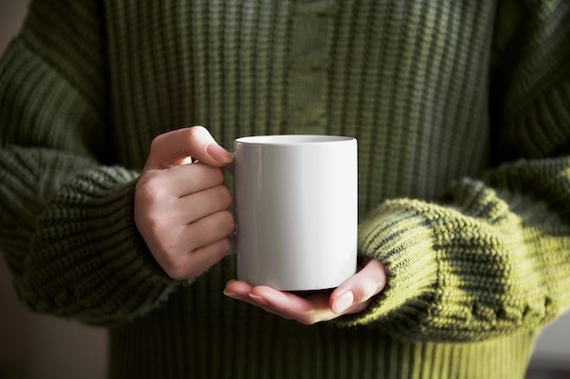 Girl in green sweater holding white porcelain mug mock up