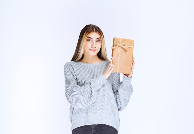 Girl in grey sweater holding a cardboard gift box.