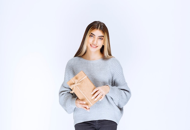 Girl in grey sweater holding a cardboard gift box.