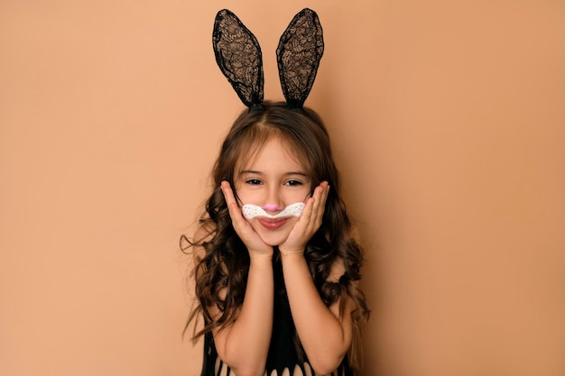 Girl in guise of an Easter bunny holds her cheeks with hands smiling sweetly