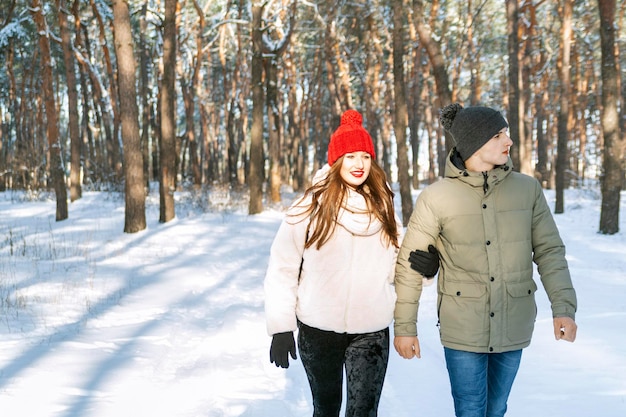 Girl and guy are walking in the winter park. Young couple in snowy forest.