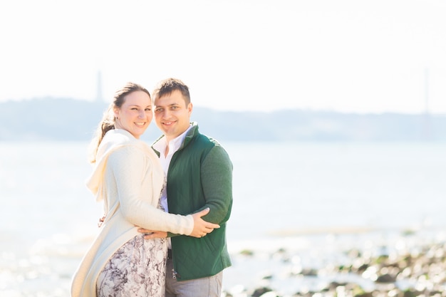 Girl and guy hugging and looking at the camera lens on the river bank on a sunny day