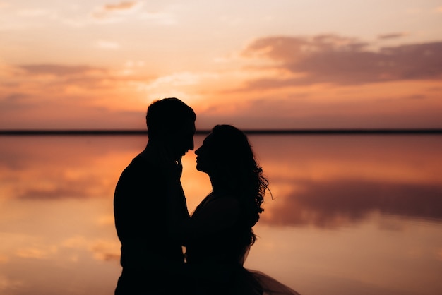 Girl and a guy on the shore of a pink salt lake at sunset