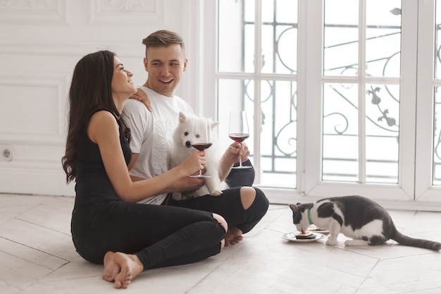 A girl and a guy sit in a new house on the floor with their pets