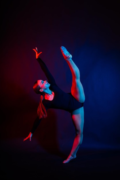 A girl gymnast in a swimsuit does tricks on a white and dark background front view