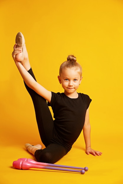 Girl gymnast trains with gymnastic clubs on yellow background. children's professional sports. Beautiful teen girl doing rhythmic gymnastics exercises