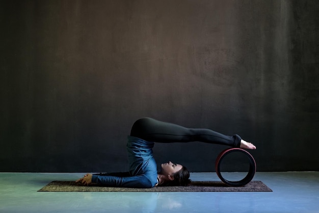 Girl in halasana pose doing yoga on black background