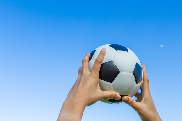 Girl hand holds a soccer ball in the sky on blue sky background.