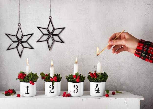 Girl hand lighting the fourth candle on a handmade advent wreath decorated with red checkerberries