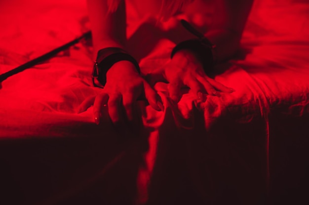 Girl hands in handcuffs and leather whip flogger for BDSM sex with submission and domination lie on bed