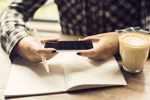 Girl hands with smartphone blank diary with pen and coffee