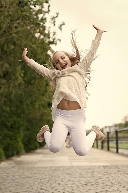 Girl on happy smiling face nature on background Happiness concept Kid girl with cheerful expression jump on international childrens day Child happy and cheerful enjoy walk in park