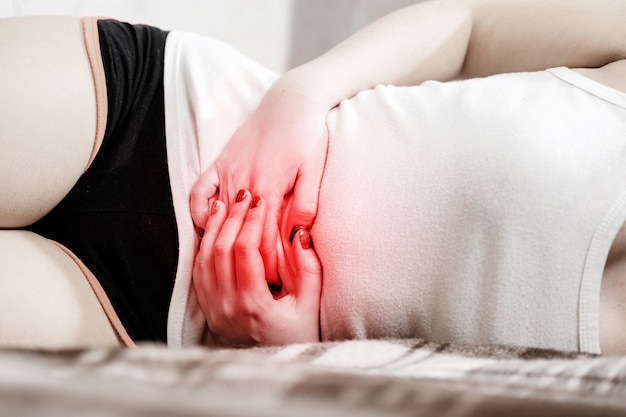 Photo girl has a stomach ache, girl is lying on the bed, red accent on the abdomen