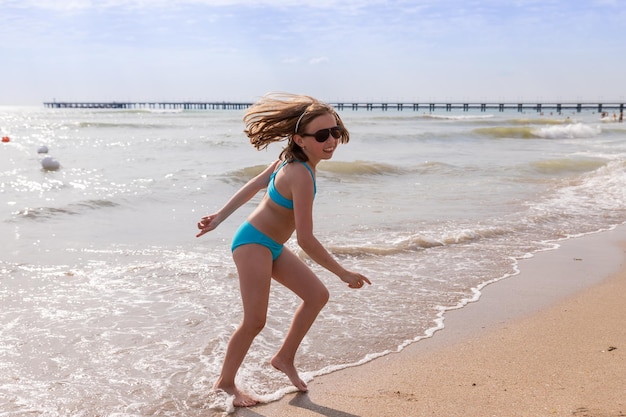 Girl has a swimsuit having fun alone on the sand in summer by the sea female child dancing by the wa