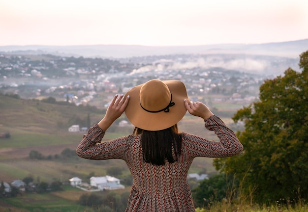 Girl in hat from behind looks at the city at sunset