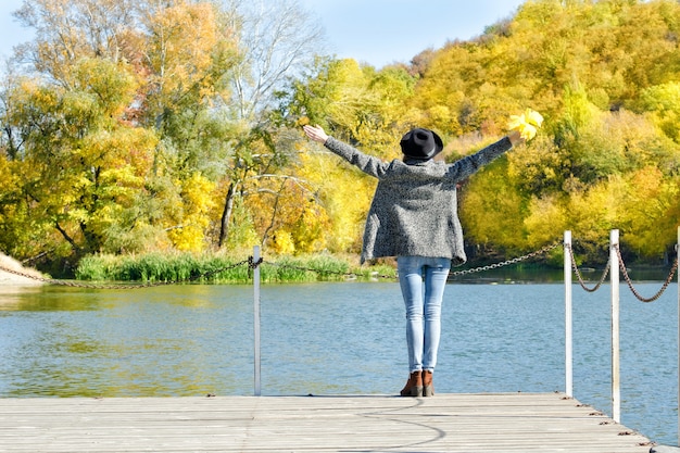 Girl in the hat is standing on the dock with her hands up.