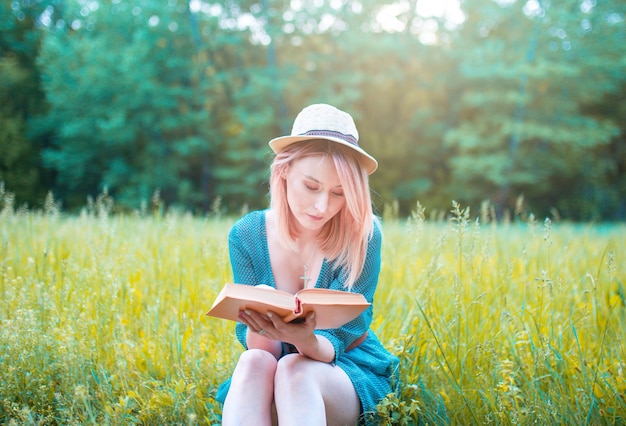 Girl in a hat reads a book in the fresh air.