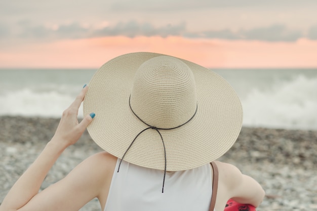 Girl in a hat sits by the sea