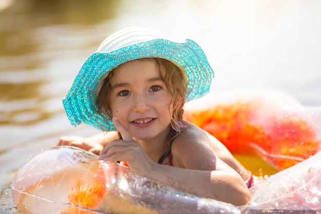 Girl in a hat stands on the river bank with a transparent inflatable circle in the shape of a heart with orange feathers inside Beach holidays swimming tanning sunscreens