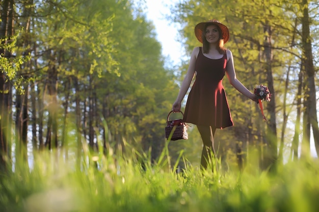 A girl in a hat on a walk in the park. A girl with a basket walks in the spring. Girl is walking along the road at sunset.