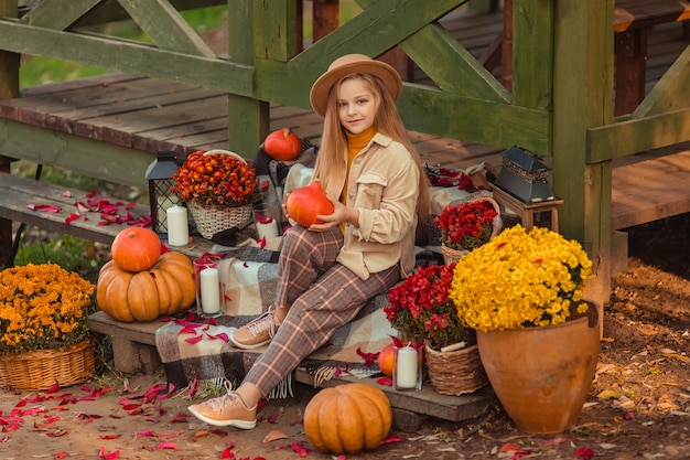 Girl in a hat with autumn decor with pumpkins and flowers