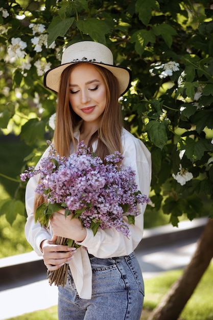 Girl in a hat with a bouquet of lilacs in the summer on a green space summer makeup. walk in the park