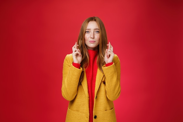 Girl having faith everything be fine cross fingers for good luck as supplicating, making wish looking hopeful at camera anticiapting miracle and dream come true against red background.