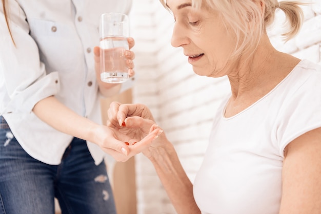 Girl helps old woman drink pills.