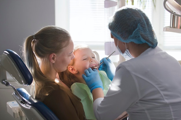 Girl, her mom and the dentist in the dental office, the stomatologist examining and consulting, daughter playing and complaining, health care since childhood