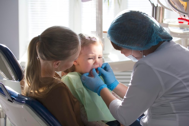 Girl, her mom and the dentist in the dental office, the stomatologist examining and consulting, daughter playing and complaining, health care since childhood