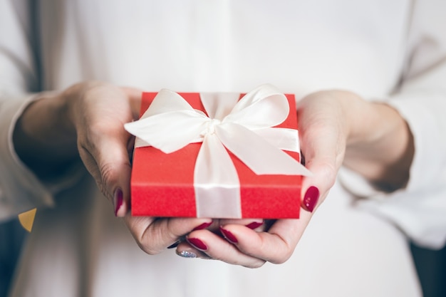 Girl holding beautiful  gift for the day valentines day. red box and white bow and bokeh in the background