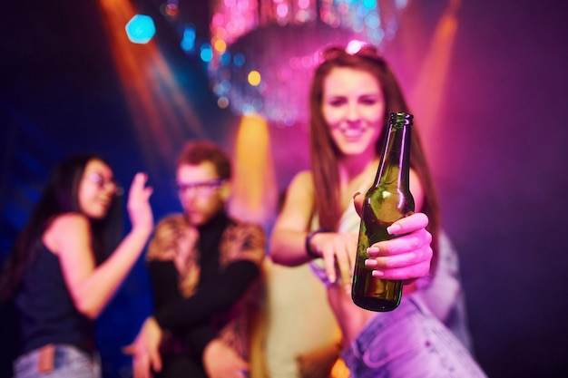 Girl holding bottle Young people is having fun in night club with colorful laser lights