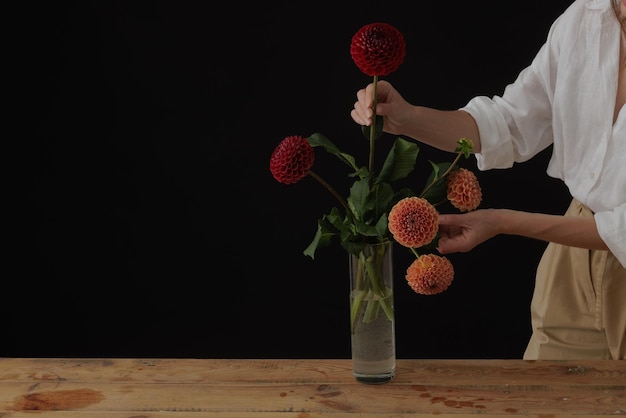 Girl holding a dahlia flower in a glass vase on a wooden table dark background mockup