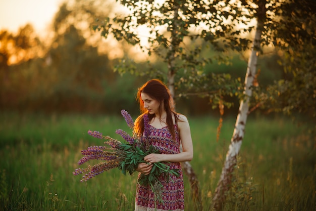 Girl holding flowers. Brunette in field. sunset