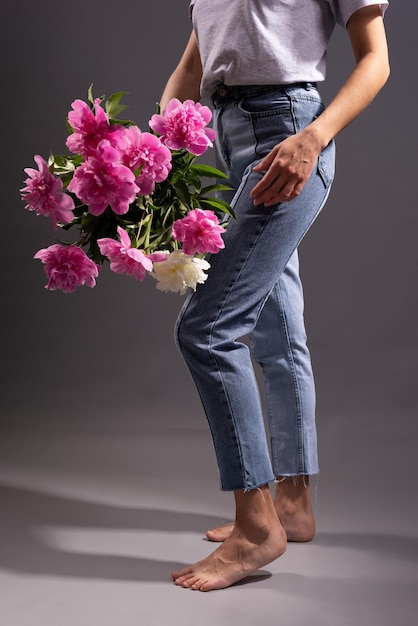 Girl holding flowers in denim pants, on a gray background.