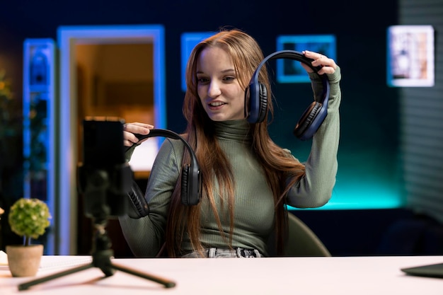 Girl holding headphones in hands filming with smartphone on tripod