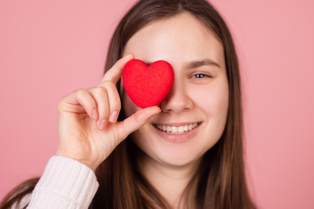 Girl holding a heart in her hands closeup on a pink background the concept of valentine's day