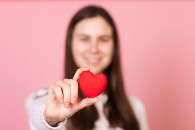 Girl holding a heart in her hands closeup on a pink background the concept of valentine's day