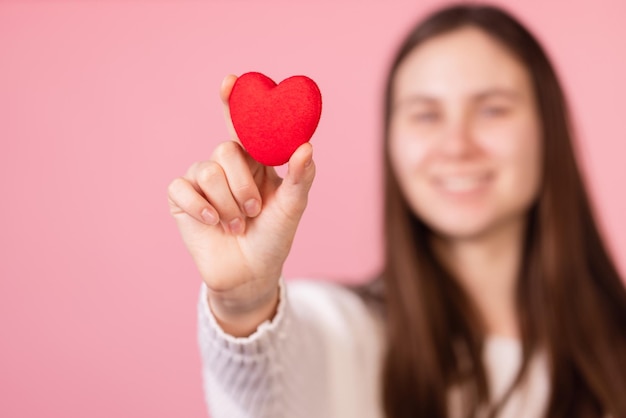 Girl holding a heart in her hands closeup on a pink background the concept of valentine's day