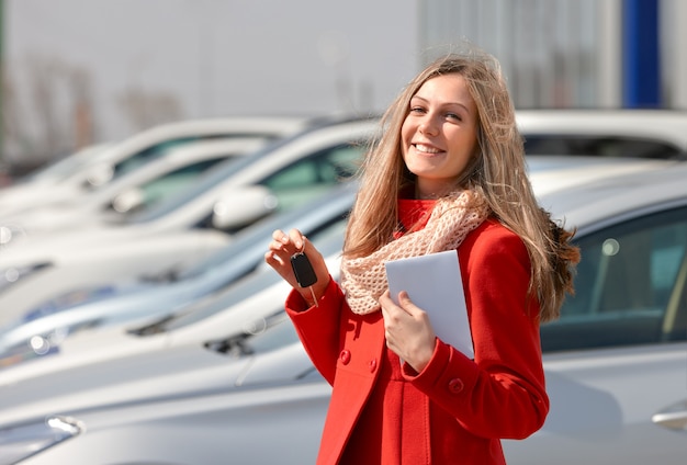 Girl holding the keys in his hand on a background of salon cars for sale