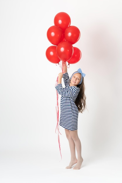 Girl holding large bunch red balloons in hands smiling and looking at camera on white background