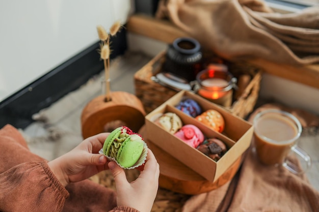 Girl holding a macaron in her hand with a box of assorted macarons in the background in a cozy home atmosphere