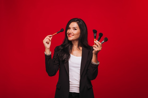 Girl holding makeup brushes on red background