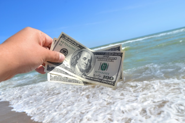 Girl holding a money bill of 300 dollars on background of sea waves