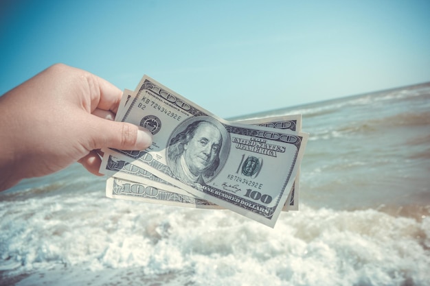 Girl holding a money bill of 300 dollars on background of sea waves