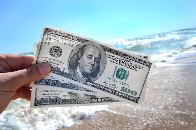 Girl holding a money bill of 300 dollars on background of sea waves